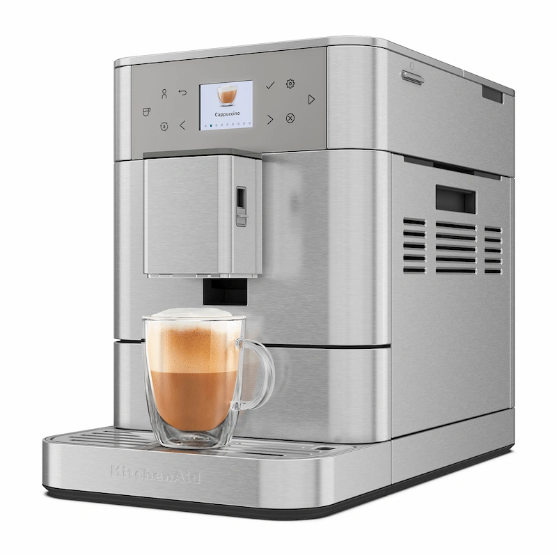 Vista 3/4 de la cafetera superautomática KitchenAid KF6 preparando un cappuccino con espuma de leche densa en una cocina moderna.