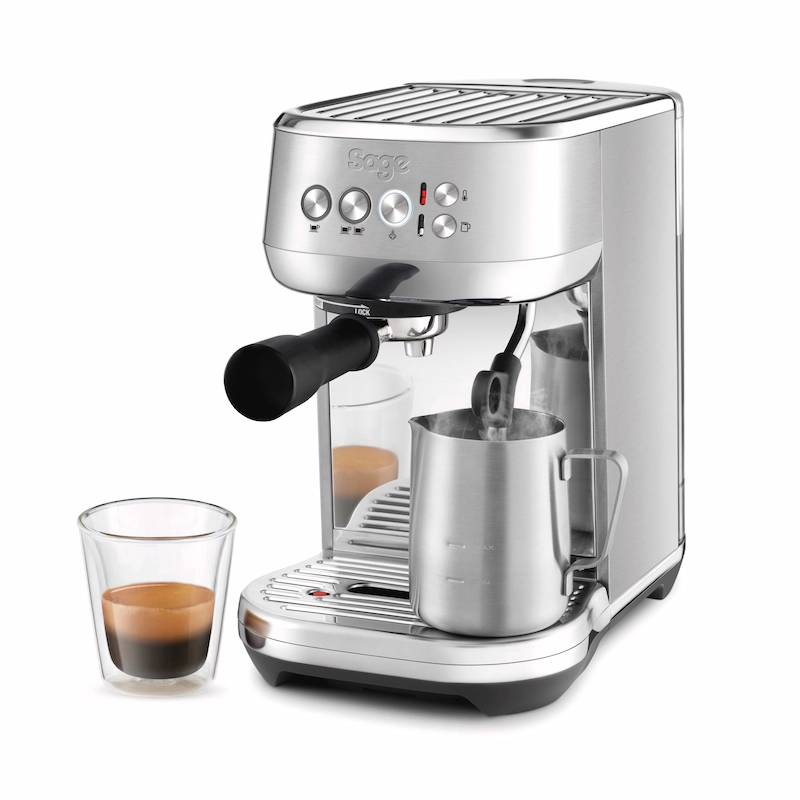 Cafetera Sage Bambino Inox con un espresso recién servido y vaporizador texturizando leche en jarra de acero.