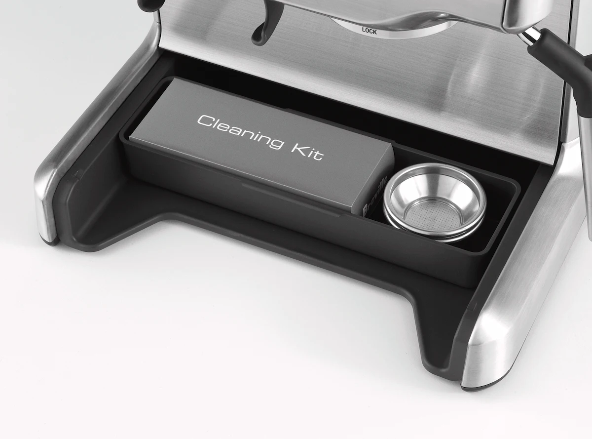 Compartimento oculto con el kit de limpieza bajo la base de la cafetera Sage Barista Express para mantenimiento de café de especialidad.